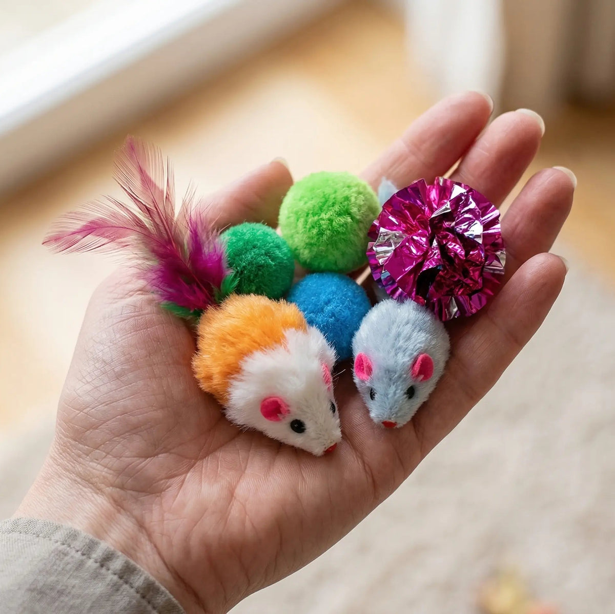 Main présentant les petites souris en peluche et les balles sonores colorées, au format idéal pour la morsure d'un chat.