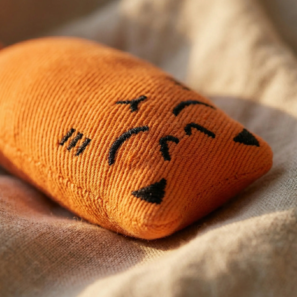 Gros plan sur les coutures résistantes et le visage souriant brodé du jouet en peluche orange pour chat.