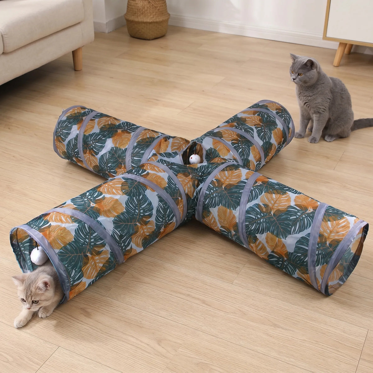 Chat gris d'intérieur observant attentivement l'une des entrées de son grand tunnel de jeu 4 voies à motifs feuilles végétales.